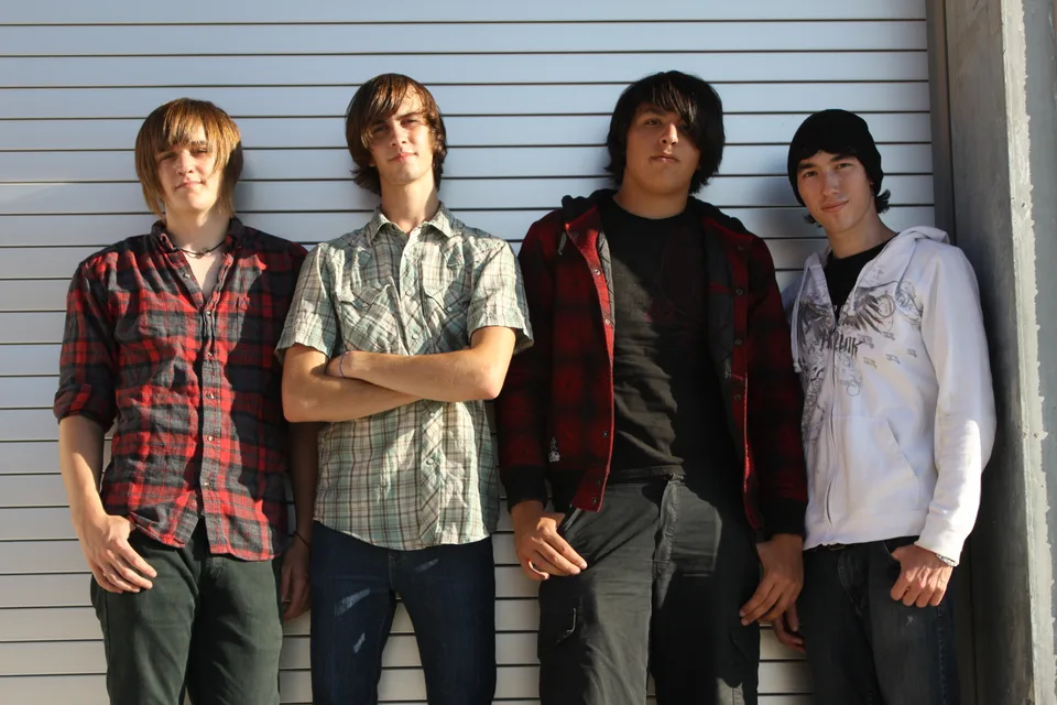 Four band members standing together in front of a garage door.