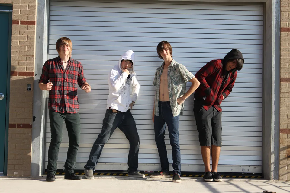 Four band members striking different poses in front of a garage door.