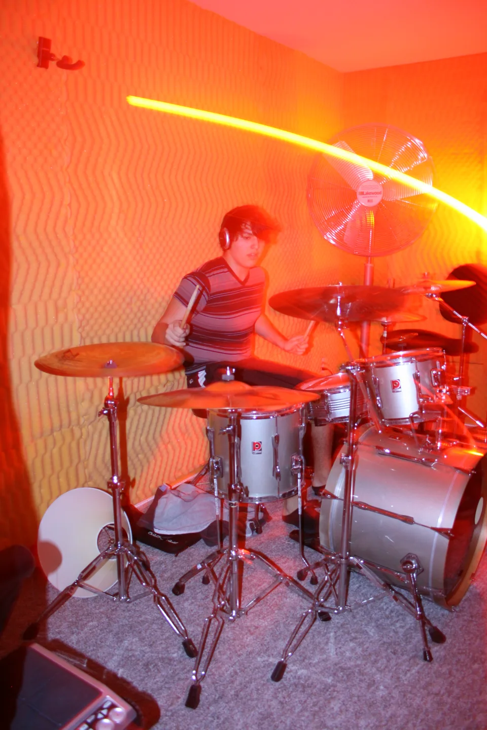 A drummer wearing headphones, surrounded by a drum kit and orange light trails.