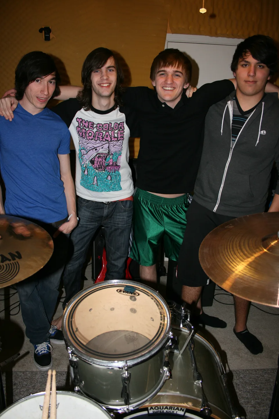 Four band members posing together behind a drum kit.