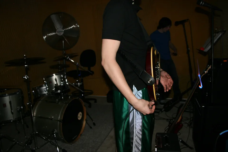 A close view of a guitarist in green shorts beside a drum kit.