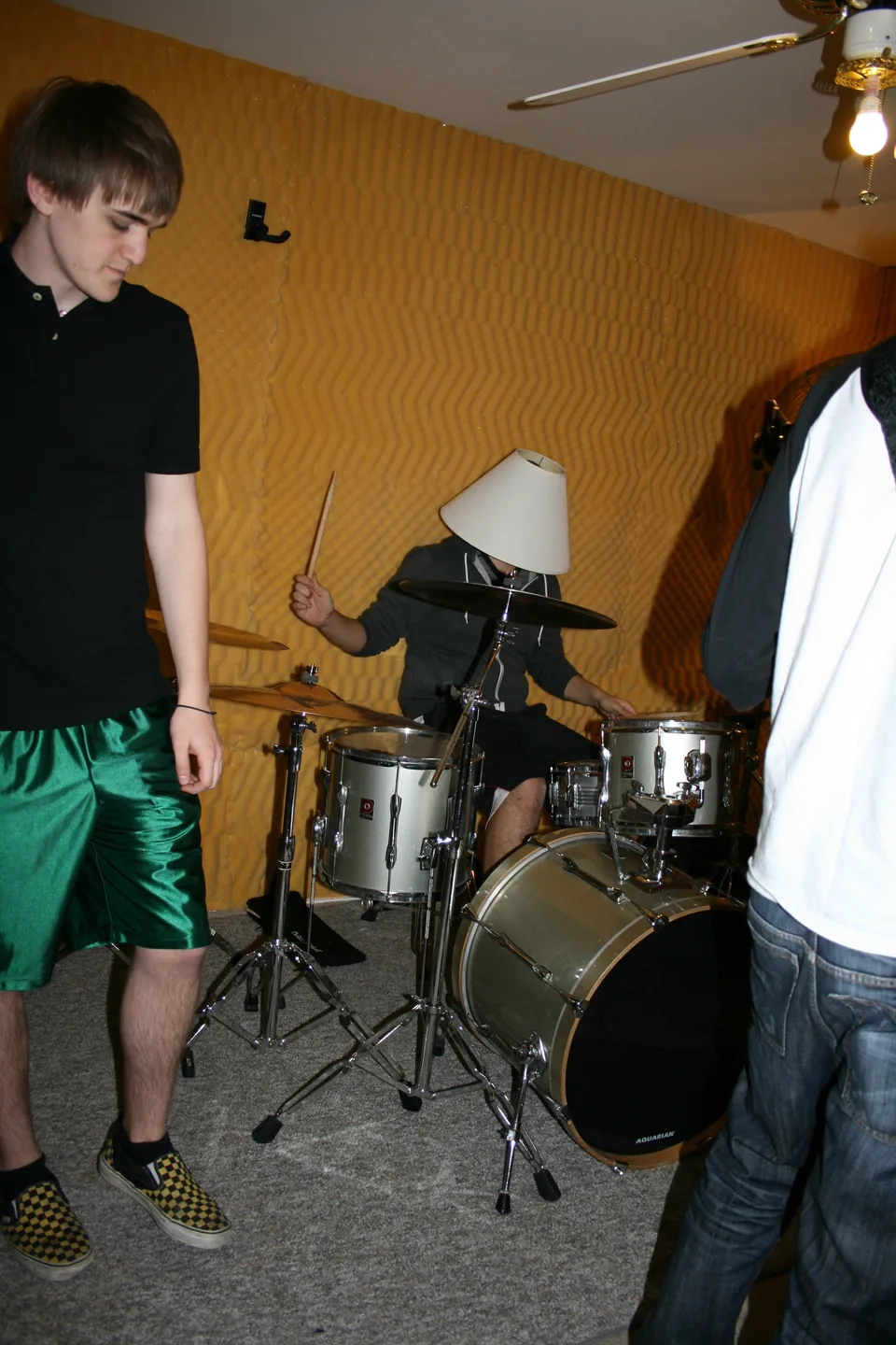 A drummer with a lampshade over his head, between two band members.