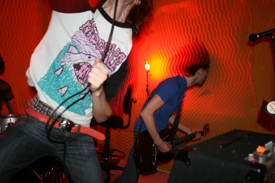 A vocalist in the foreground and a guitarist behind him, surrounded by orange light trails.