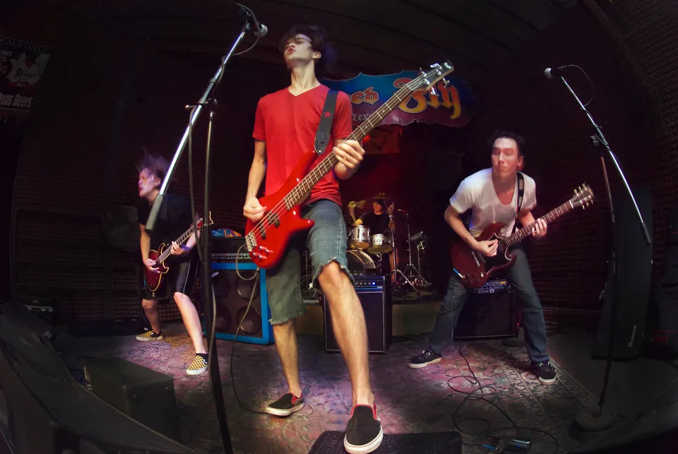 A bassist at a microphone, with two guitarists and a drummer performing behind him.