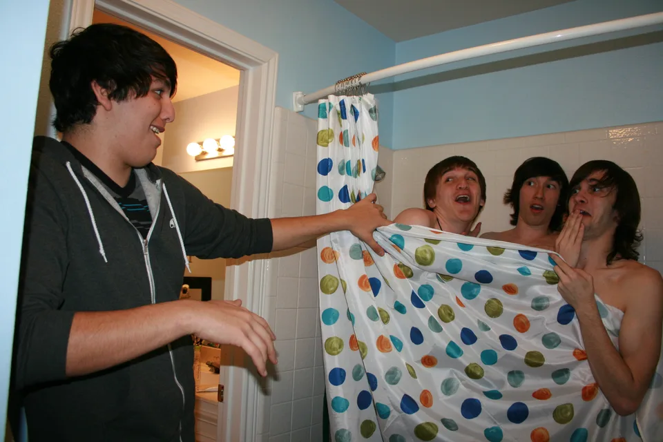 A band member pulls back a shower curtain as three others pose behind it.
