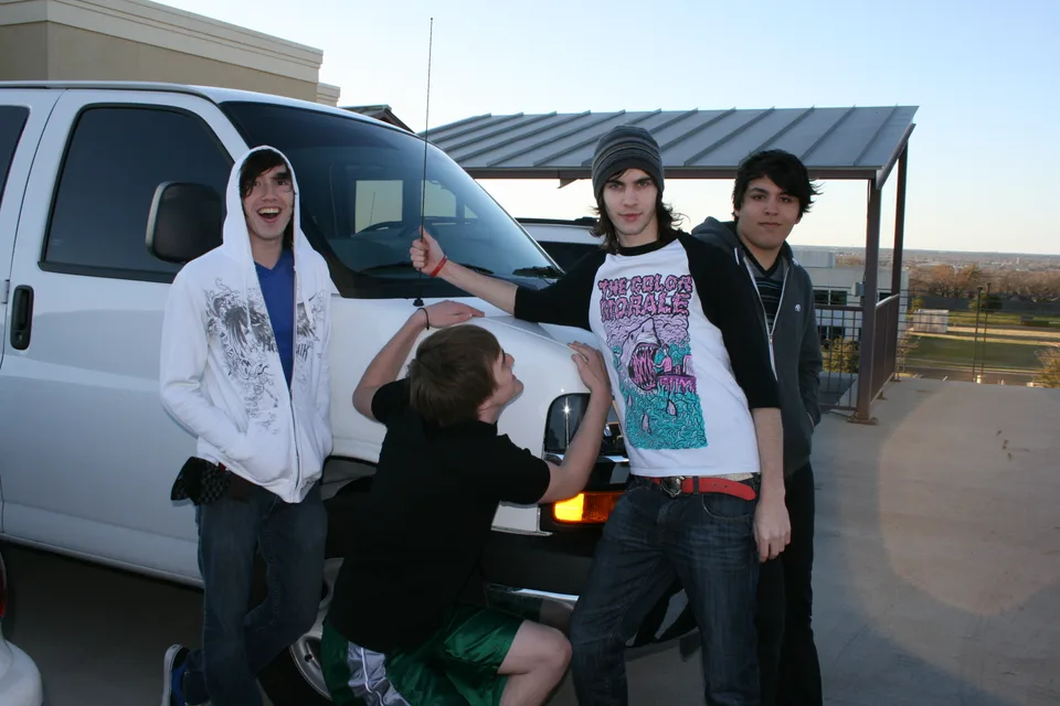 Four band members posing around the front of a white van.